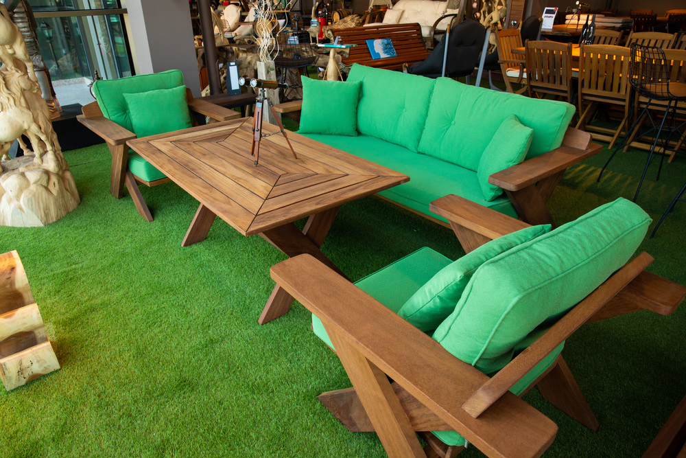 Conjunto de muebles de jardín de madera con cojines verdes vibrantes, compuesto por un sofá, dos sillones individuales y una mesa de centro de diseño rústico, colocado sobre césped artificial en un espacio decorado con elementos de madera natural.